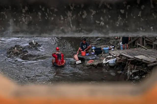 Sebuah keluarga menjalani aktivitas sehari-hari di sungai yang tercemar, mencuci pakaian, dan mandi, di Jakarta.