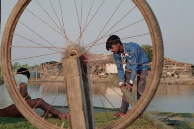 높은 대나무 기둥 위에 자전거 바퀴 테두리를 달고, 줄을 사용해 대나무를 건물에 고정한다