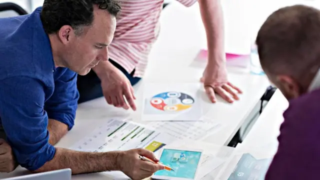 Tres personas discutiendo sobre papeles en una mesa de trabajo