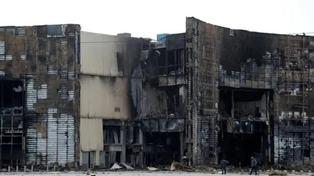 युद्ध में क्षतिग्रस्त हुई एक इमारत के पास से गुजरते कुछ लोग