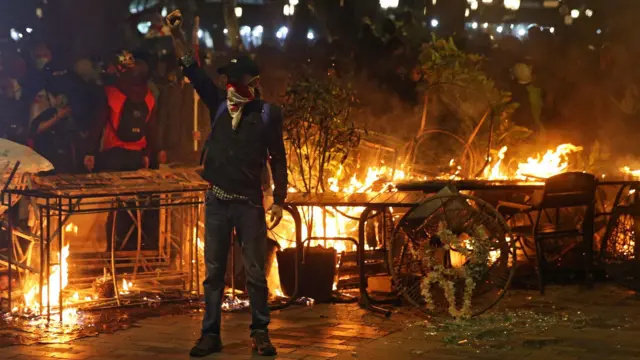 Демонстрант стоит с поднятым кулаком на фоне горящей баррикады