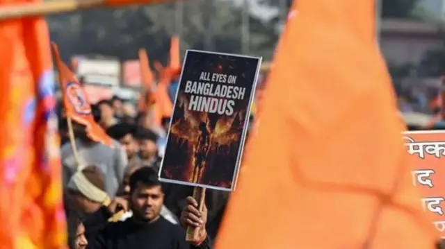 भारत में बांग्लादेश के ख़िलाफ़ प्रदर्शन में एक हाथ तख़्ती उठाए हुए जिसमें लिखा है सभी आँखें अब बांग्लादेश के हिंदुओं पर हैं 