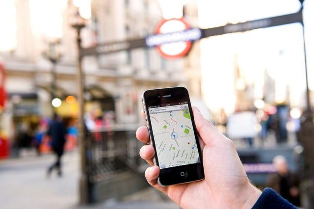 Hombre sostiene un iPhone en el que tiene activado Google Maps en una calle de Londres.