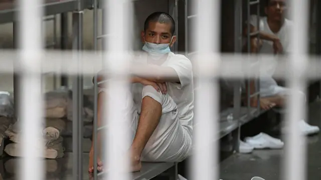 鉄格子越しに、ベッドに座っている収容者を写した写真