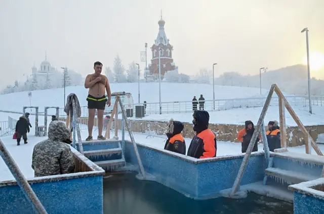 Човек се припрема да скочи у ледену воду док спасиоци стоје у близини током прославе православног хришц́анског празника Богојављања у сибирском граду Краснојарску, Русија, у јануару 2026.