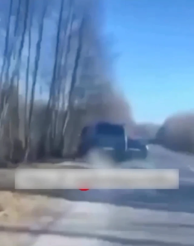 Мікроавтобус стоїть на узбіччі поруч із лісосмугою, з правого боку його притискає легкове авто. Зображення трохи розмите, ніби зняте з руху.