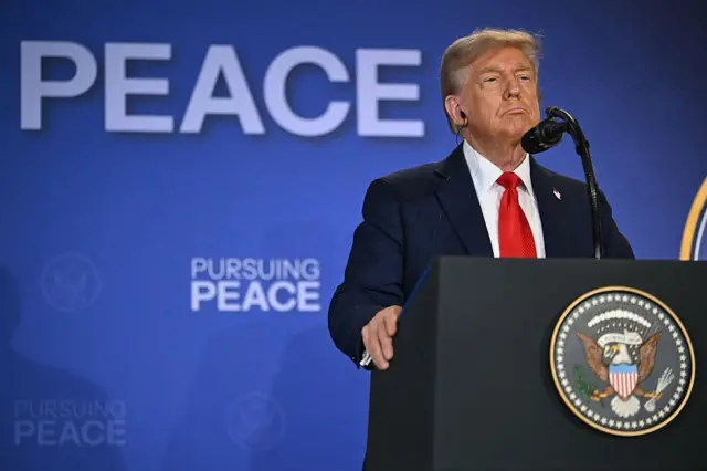 Donald Trump diante de um microfone em um púlpito com o símbolo da Casa Branca e uma faixa atrás dele que diz 'em busca da paz'