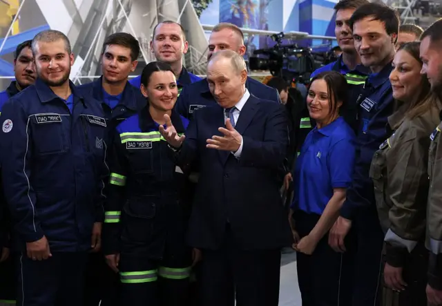 Владимир Путин что-то весело рассказывает рабочим Магнитогорского металлургического комбината, те льстиво улыбаются