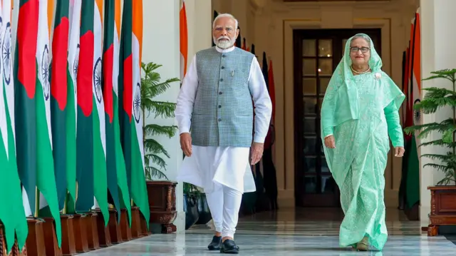 ২০২৪ সালে ভারতের প্রধানমন্ত্রী নরেন্দ্র মোদীর সঙ্গে একটি বারান্দা দিয়ে হেঁটে আসছেন বাংলাদেশের তৎকালীন প্রধানমন্ত্রী শেখ হাসিনা। নরেন্দ্র মোদীর পাশে ভারত ও বাংলাদেশের বেশ কিছু পতাকা। 