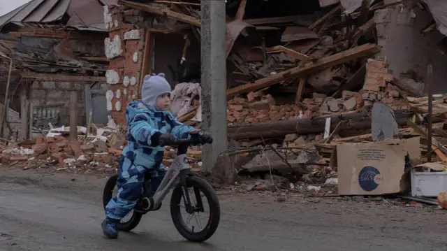 Дитина їде на велосипеді біля зруйнованих будинків у Золочеві, Харківська область