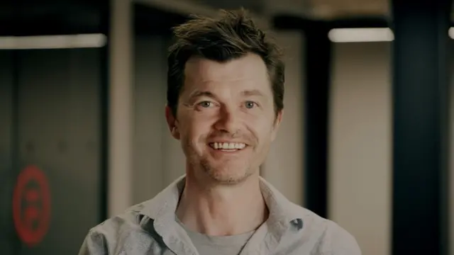 스콧 만이 캐주얼한 복장으로 미소 짓고 있다.