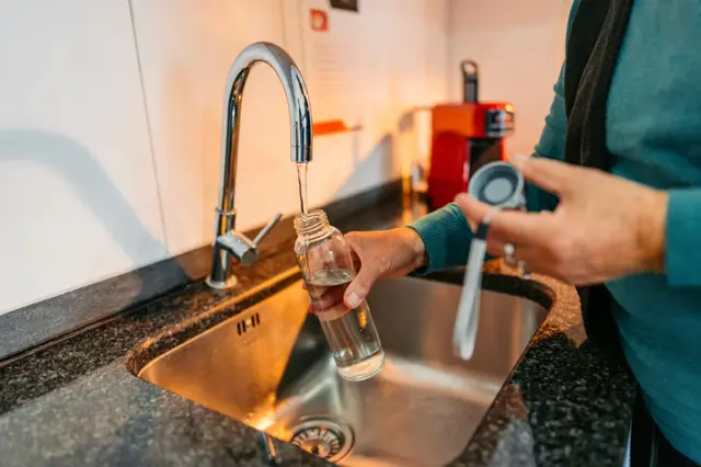 Seseorang mengisi ulang botol airnya dengan air dari keran di dapur rumah.