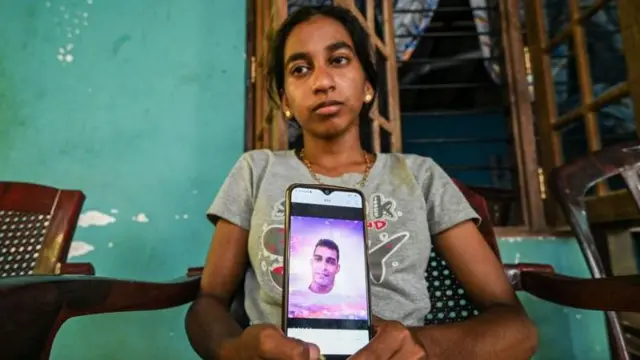 Piumi Lakshani, daughter of the protestor who was reportedly shot a day earlier by the police during an anti-government demonstration, holds a mobile phone displaying a picture of her father at her residence in Rambukkana on April 20, 2022