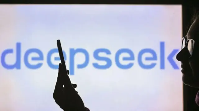 ظل امرأة تمسك بهاتف وفي الخلفية مكتوب باللون الأزرق على شاشة بيضاء ديب سيك بالإنجليزية