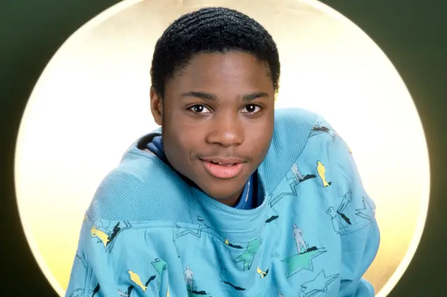 Malcolm-Jamal Warner wearing a light blue sweatshirt with abstract and figure patterns.