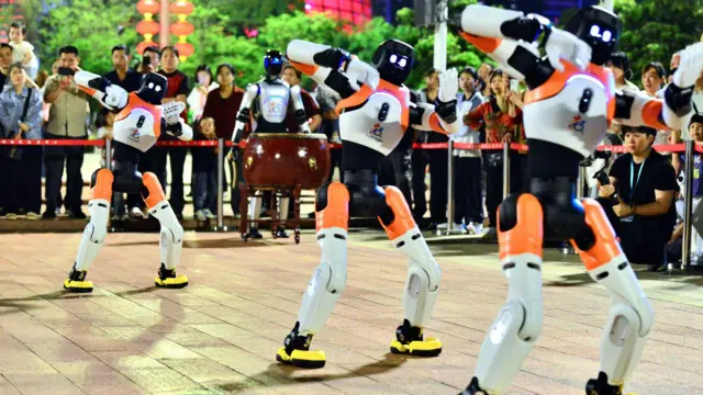 Bir grup robot, izleyen kalabalık önünde senkronize şekilde hareket ediyor.