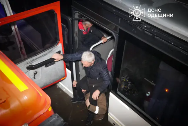 Рятувальник переносить на плечах жінку з автобуса до автомобіля ДСНС, стоячи по пояс у воді