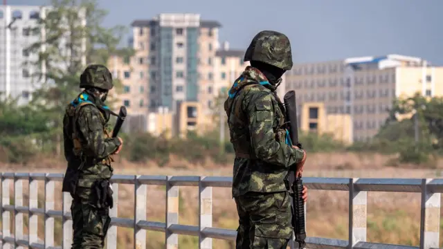 Dos soldados tailandeses vigilan desde un puenta, conlos edificios del lado birmano de la frontera al fondo.