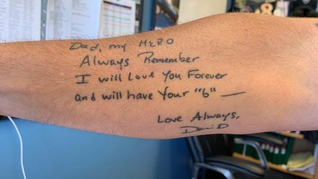 Braço de Dave Betz's, com tatuagem de mensagem que o filho escreveu no Dia dos Pais, na qual chama o pai de heroi e diz que vai amá-lo para sempre.