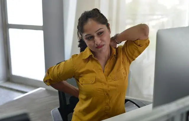 এক নারী ঘাড়ে ও কোমরে হাত দিয়ে বসে আছে।