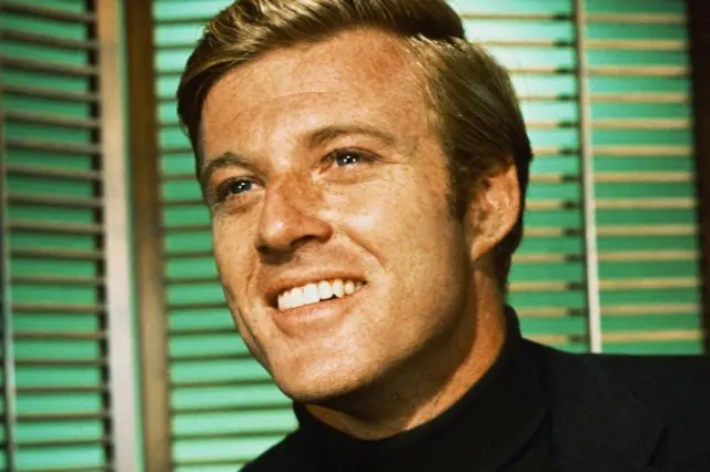 On voit Robert Redford dans la vingtaine. Il sourit radieusement et regarde vers la gauche. 