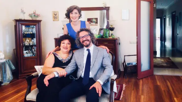 Rezzan Ebubekir oğluyla birlikte bir salonun ortasında koltukta oturuyor. Arkada kızı ayakta duruyor. 