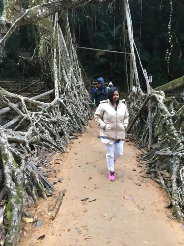 உயிர் வேர்ப் பாலத்தில் நடந்து வரும் ஒரு பெண் சுற்றுலாப் பயணி.