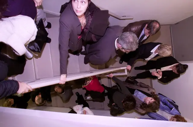 사람들이 한 줄로 계단을 내려가고 있다. 한 사람은 시계로 시간을 재고 있다.