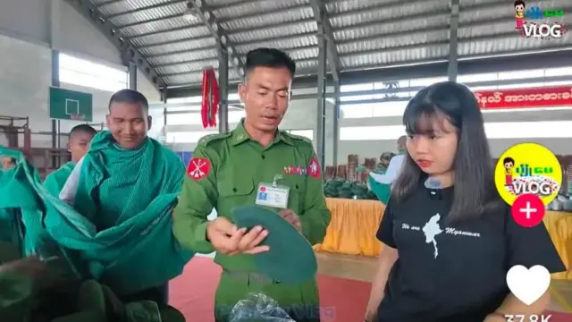 တီရှပ်အနက်ရောင်နဲ့ လူငယ်အမျိုးသမီးတစ်ဦးကို စစ်အသုံးအဆောင်ကိုင်ပြီးရှင်းပြနေတဲ့ စစ်သားတစ်ဦး။ သူတို့နောက်မှာရပ်နေတဲ့ စစ်စောင်ပါးကို အိတ်လိုလုပ်လွယ်ထားတဲ့ တပ်သား ၂ ဦး