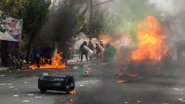 Police officers in riot gear walk past a fire, outside a court, where the trial of leaders and members of the Golden Dawn far-right party takes place in Athens