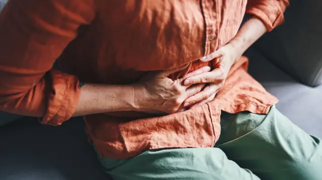 Una persona sentada, a la que no le vemos el rostro, se agarra el abdomen en señal de dolor