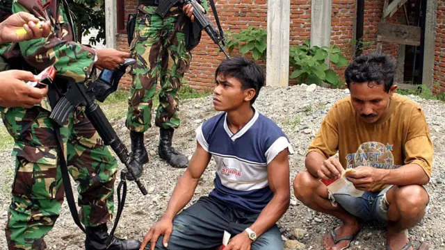 Tentara Indonesia memeriksa kartu identitas dua warga Aceh setelah baku tembak antara tentara Indonesia dan GAM di Aceh Besar, pada 16 Agustus 2003.
