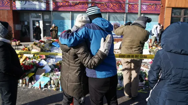 Dvoje ljudi se teše 26. januara 2026. godine kod mesta gde su ICE agenti ubili Aleksa Pretija. Cveće i sveće su položeni iza žute policijske trake 