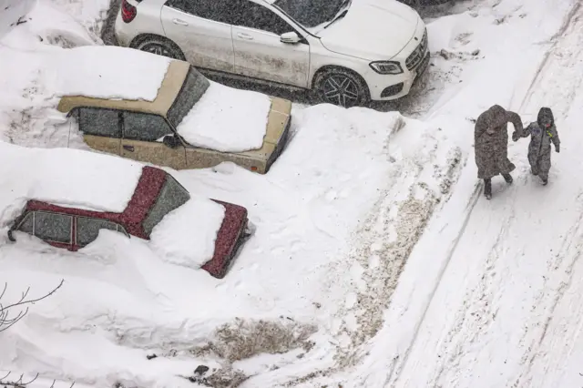 Женщина с ребенком идет мимо занесенных машин