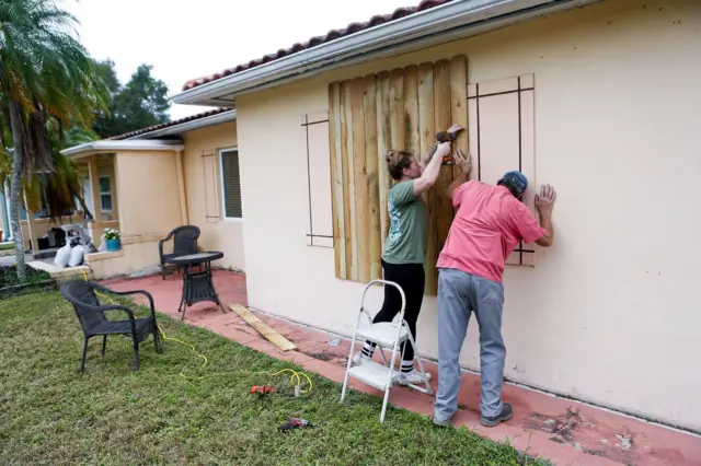 Duas pessoas afixando na parede externa de casa proteção com madeira perto das janelas