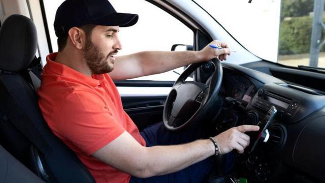 homem sentadocasa de aposta deposito 1 realbanco do motorista, com camiseta vermelha, mexecasa de aposta deposito 1 realcelular posicionado no painel do carro