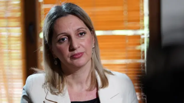 Selvi Izeti sitting in a chair wearing a white jacket - she has shoulder-length blonde hair