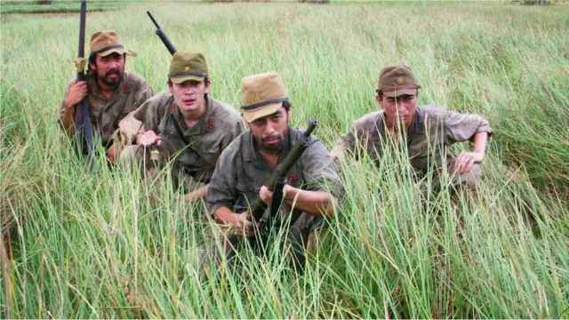 Homensroleta decisivauniforme militar seguram espingardas e estão agachadosroleta decisivameio ao mato