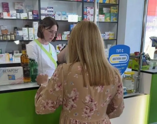 Жінка у квітчастій сукні стоїть в аптеці