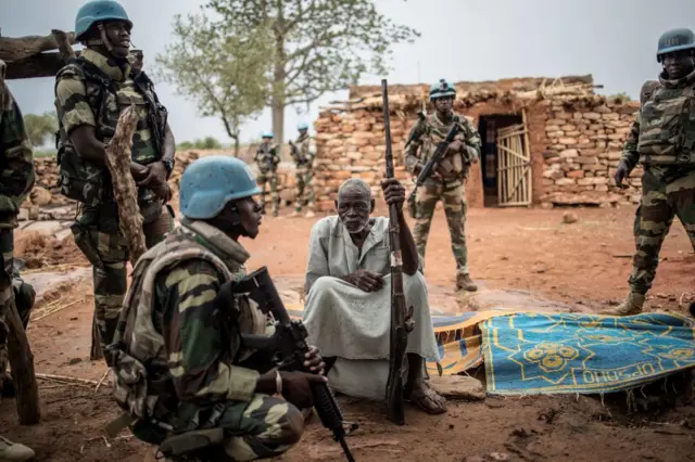 Salifu Dibo (C), agriculteur dogon et chef de la communauté de So, dans la région dogon du centre du Mali, est assis avec son fusil de chasse alors qu'il est accueilli par un soldat sénégalais de la 2e compagnie mécanisée du bataillon sénégalais de la MINUSMA (Mission multidimensionnelle intégrée des Nations unies pour la stabilisation au Mali), le 4 juillet 2019