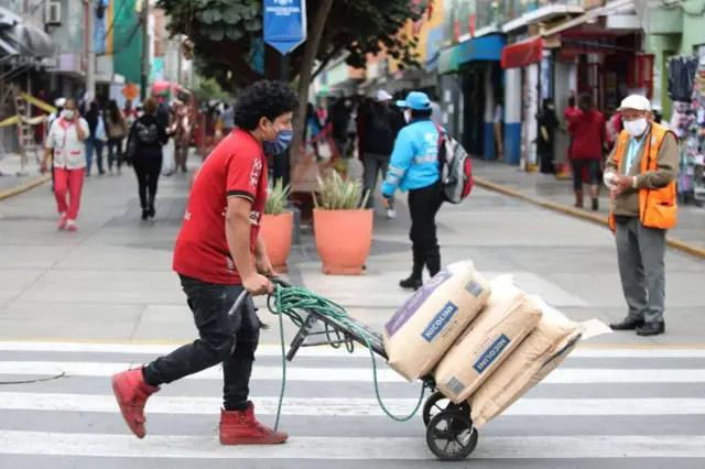 Homem empurra um carrinho carregado de sacos em uma concorrida rua de Lima, no Peru
