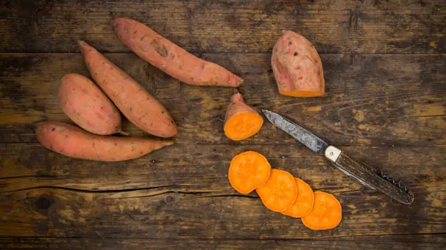 Батати та ніж на деревʼяному столі