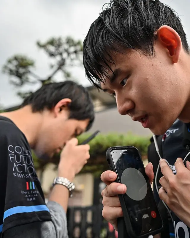 Foto tirada em 2/6/2024 mostra o jogador cego de eSports (esportes eletrônicos) Masahiro Fujimoto (à direita), conhecido como “Mashiro”, falando ao celular para usar um aplicativo com ChatGPT para obter orientações, ao lado do amigo Haruhiko Shimamura (à esquerda), no Japão