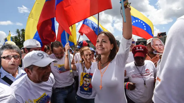 Machado (centre) marches during a demonstration in Caracas on 22 October 2016. She is with a group of political activists waving Venezuelan flags on a sunny day.