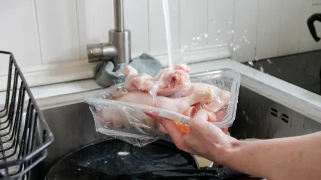 bir mutfak musluğu altında yıkanan çiğ tavuk eti. 