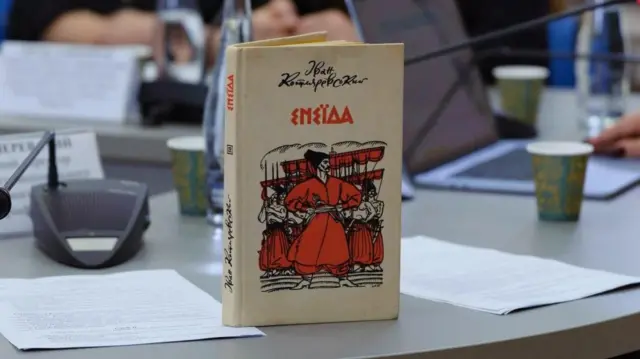 На столі - книжка, на обкладинці якої - назва та автор, Енеїда, Іван Котляревський.