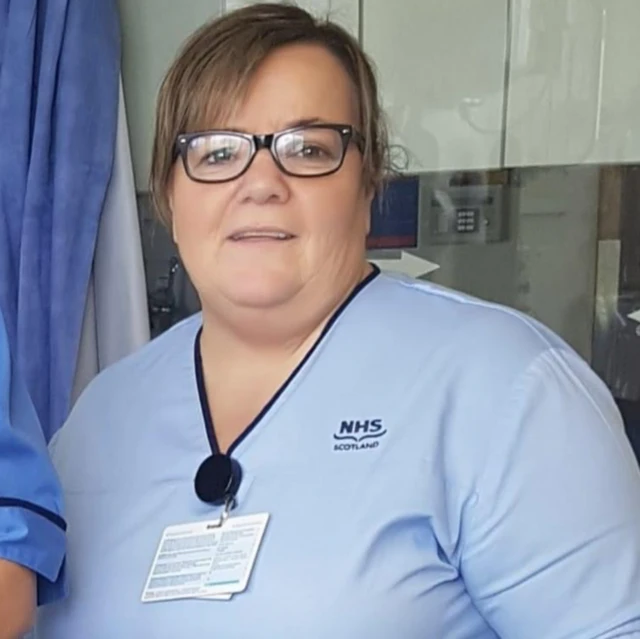 Susan McGowan sorrindo para a câmerabaixar betano oficialóculos, crachá e uniforme do hospital