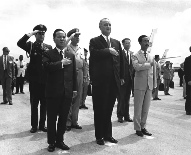 Front row, from left to right, Chairman Nguyen Van Thieu (1923 - 2001), President Lyndon B. Johnson (1908 - 1973) and Prime Minister Nguyen Cao Ky (1930 - 2011) salute during the playing of the American and Vietnamese national anthems at Guam's International Airport, Agana, March 20, 1967.