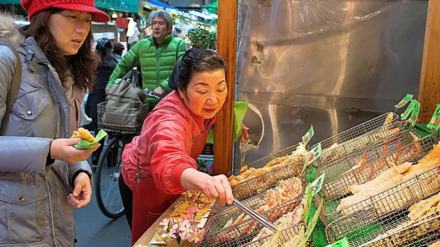 Una mujer que vende alimentos tempurizados en un mercado en Japón.