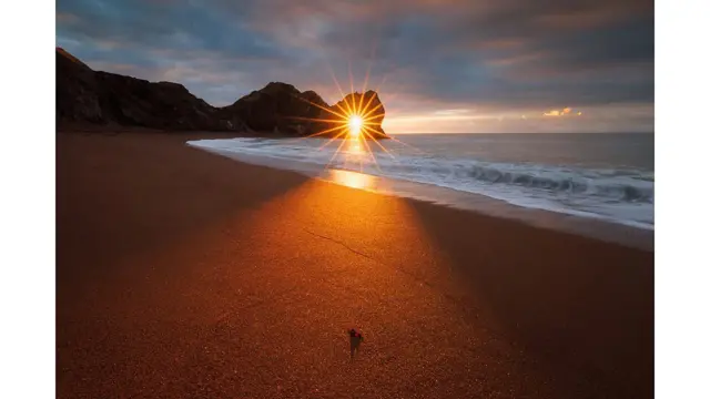 Instante en el que la luz del sol naciente pasa por la aguja de un arco de piedra caliza natural en la Costa Jurásica cerca de Lulworth en Dorset, Inglaterra.